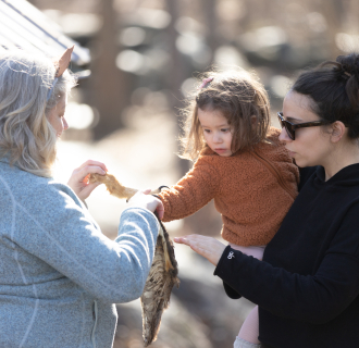 An educator shows an animal skin to a child and their caregiver.