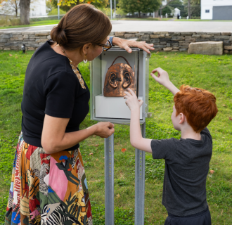 A woman and young boy opening a box with an artwork outside in the Museum's Sculpture Garden