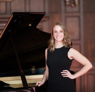 Pianist Jen Allen in a black dress standing in front of a grand piano.
