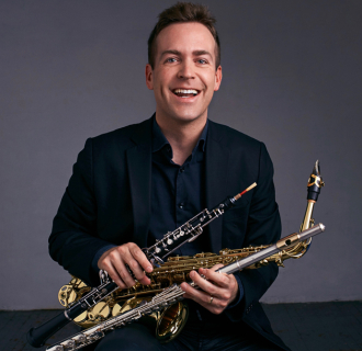 Man in a suit smiling and holding a saxophone, flute, and oboe