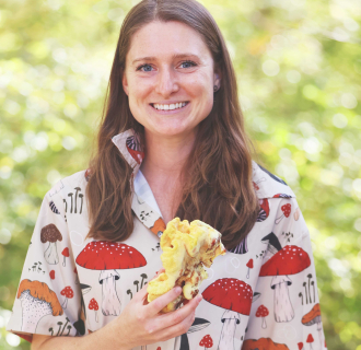 Woman holding a mushroom and wearing a shirt covered in mushroom illustrations