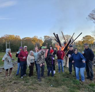 A group of people celebrating apples in an orchard, with a large fire behind them