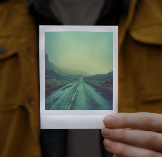 A person holding up a polaroid picture of an abandoned road.