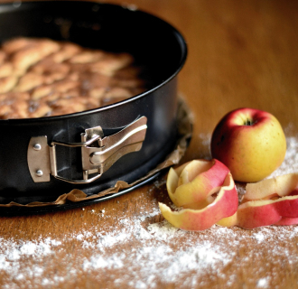 A peeled apple beside an apple cake in a springform pan