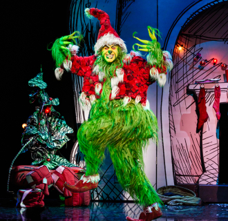 The Grinch wearing Santa clothes with a menacing look on his face.
