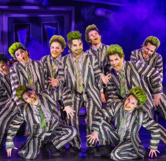 Group of male-presenting actors with green hair and striped suits on stage.