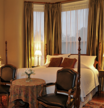 Elegant bedroom with four-poster bed, vintage chairs, and warm lighting