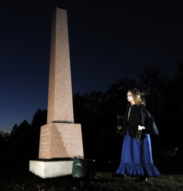 Person holding lantern near tall grave monument at night