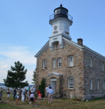 Stone lighthouse with people gathered outside near waterfront