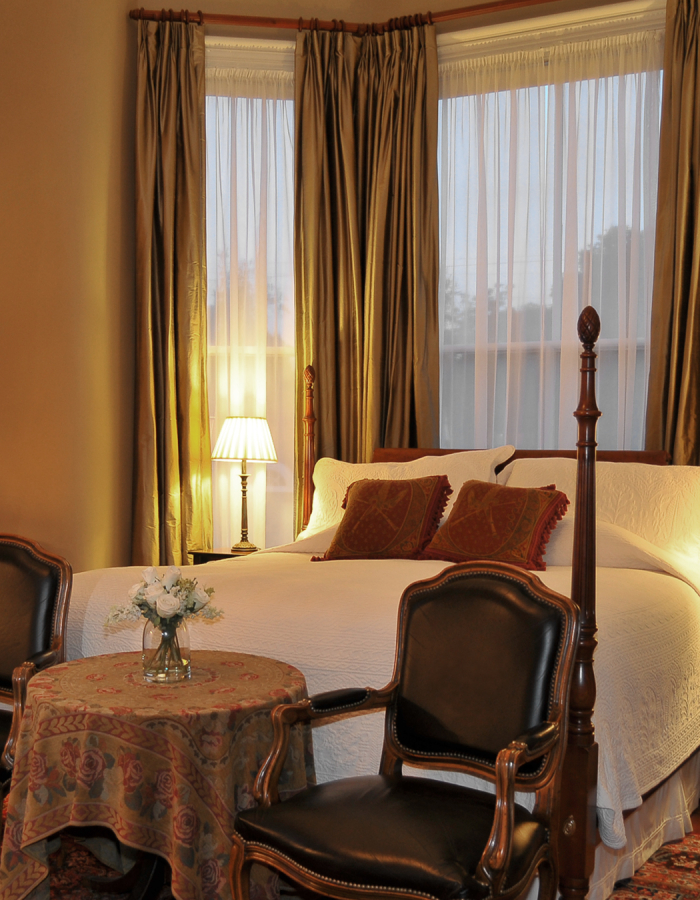 Elegant bedroom with four-poster bed, vintage chairs, and warm lighting