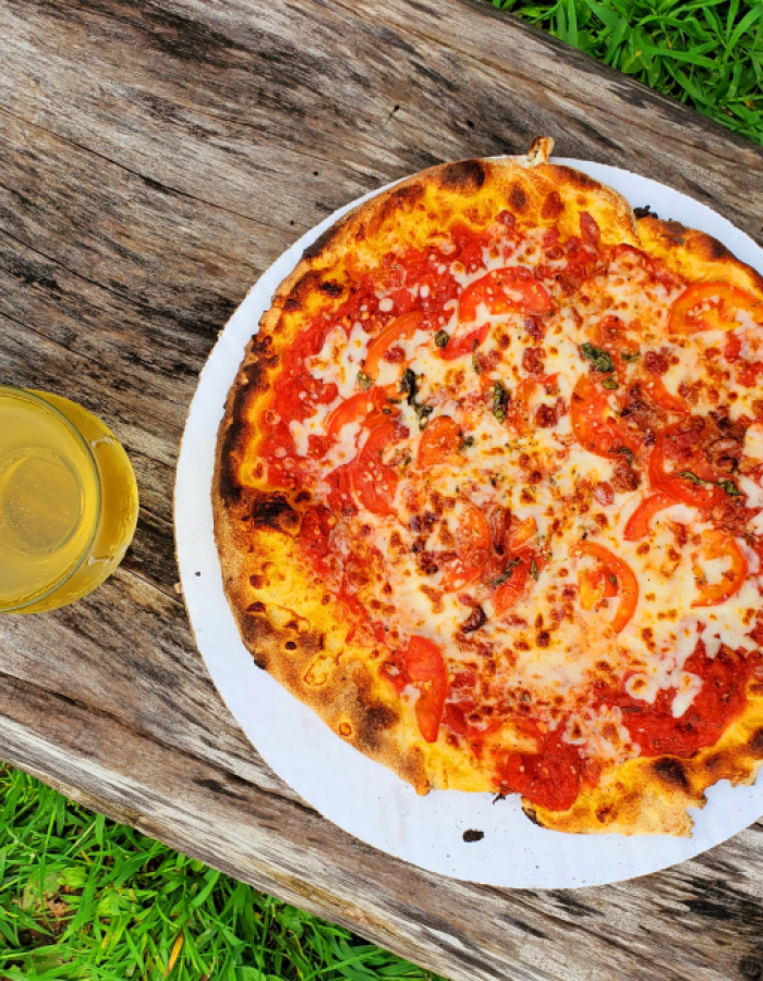 Tomato and cheese pizza on paper plate with drink on wooden table
