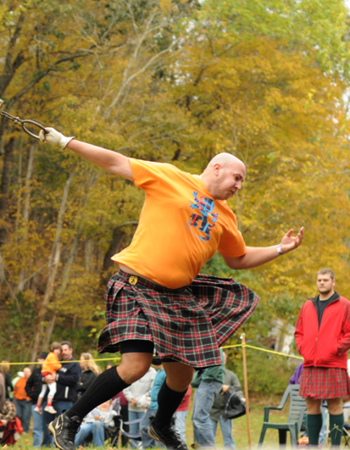 Man in kilt throwing hammer at Highland Games outdoors