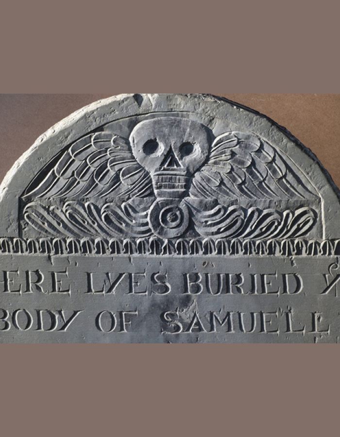 Old gravestone with winged skull carving and partial epitaph