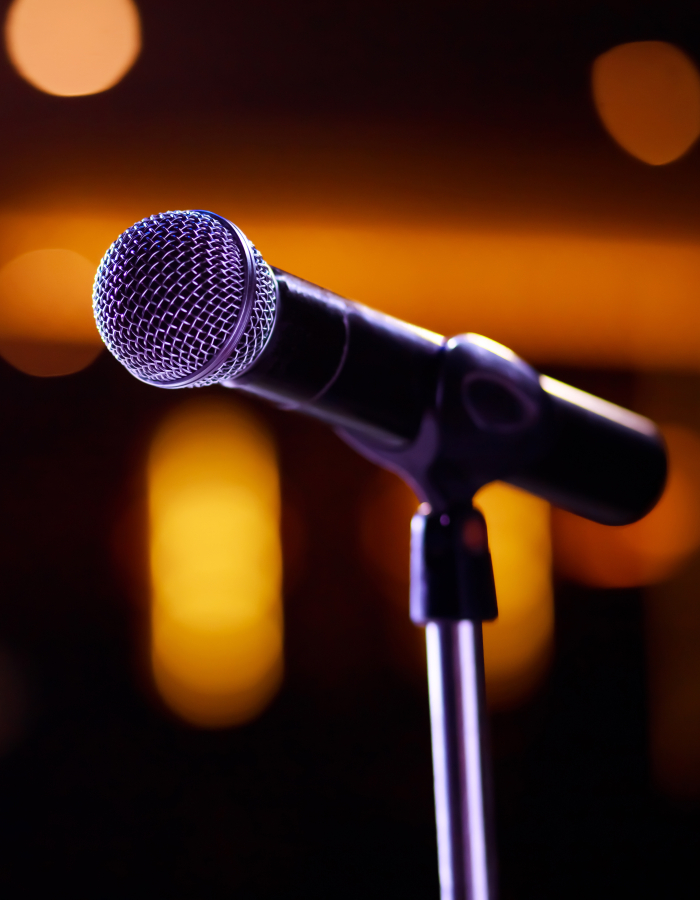 Close-up of a microphone on a stand with warm, blurred stage lights in the background.