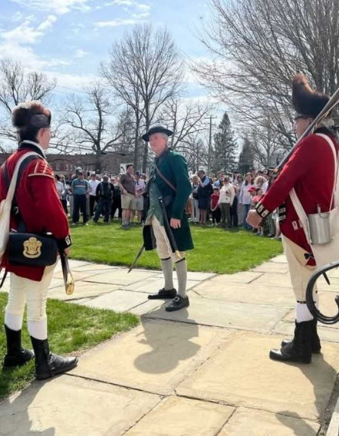 Two redcoats talking to a colonial patriot on the steps of the congregational church in Litchfield