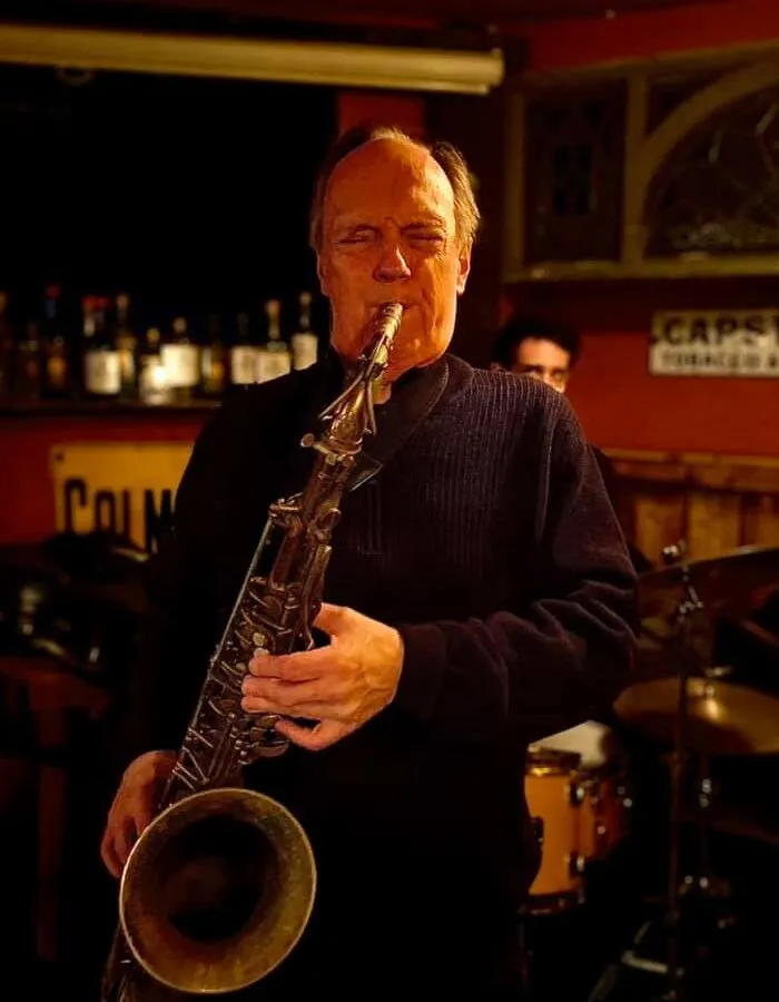A man in a navy sweater playing a barry saxophone in a cafe
