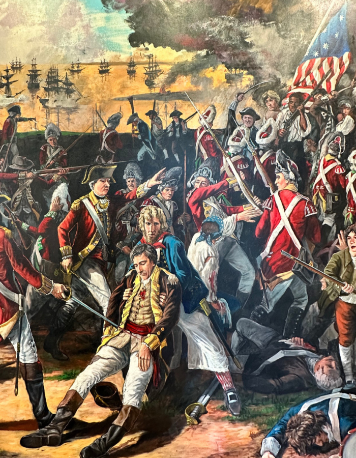 Painting of a Revolutionary War battle showing British and American forces fighting along the waterfront as a wounded officer is carried from the battlefield.