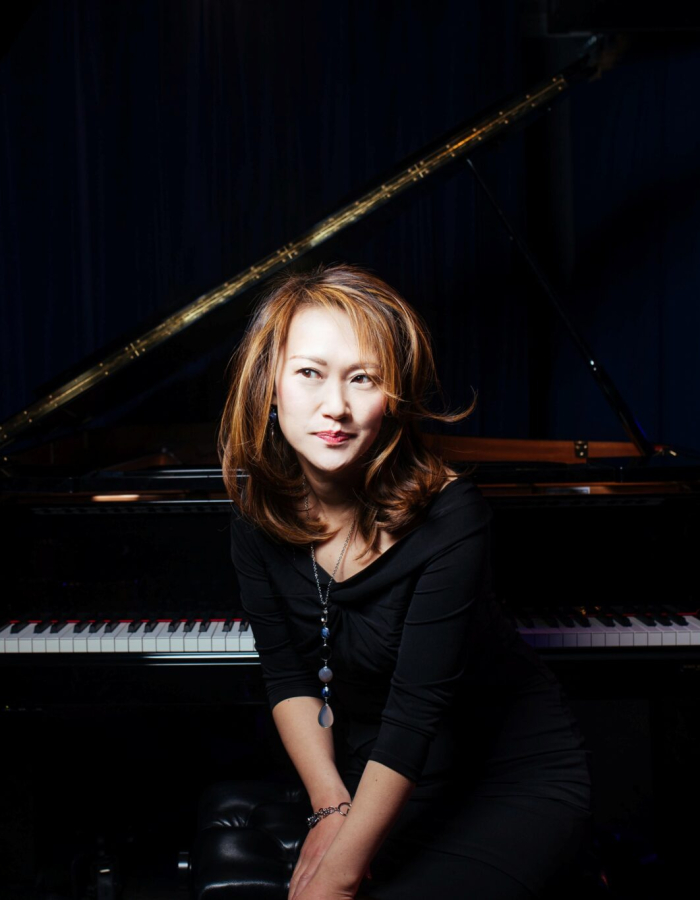 A woman in a black dress smiling in front of a grand piano