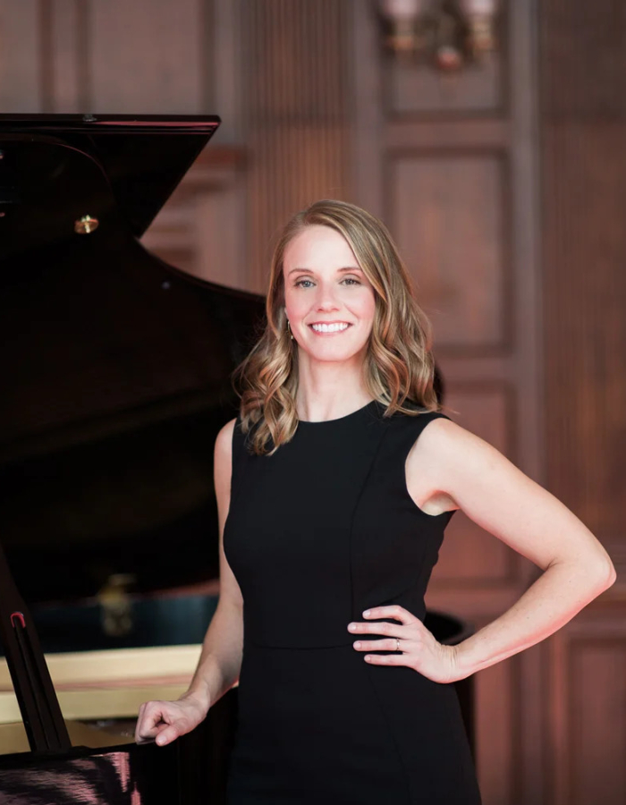 Pianist Jen Allen in a black dress standing in front of a grand piano.