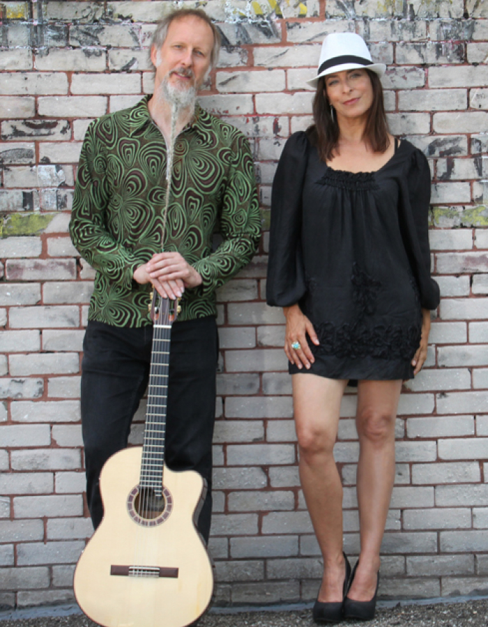 Man and woman leaning on brick wall with a guitar 