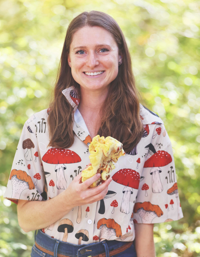 Woman holding a mushroom and wearing a shirt covered in mushroom illustrations