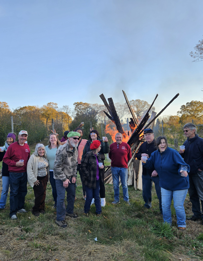 A group of people celebrating apples in an orchard, with a large fire behind them