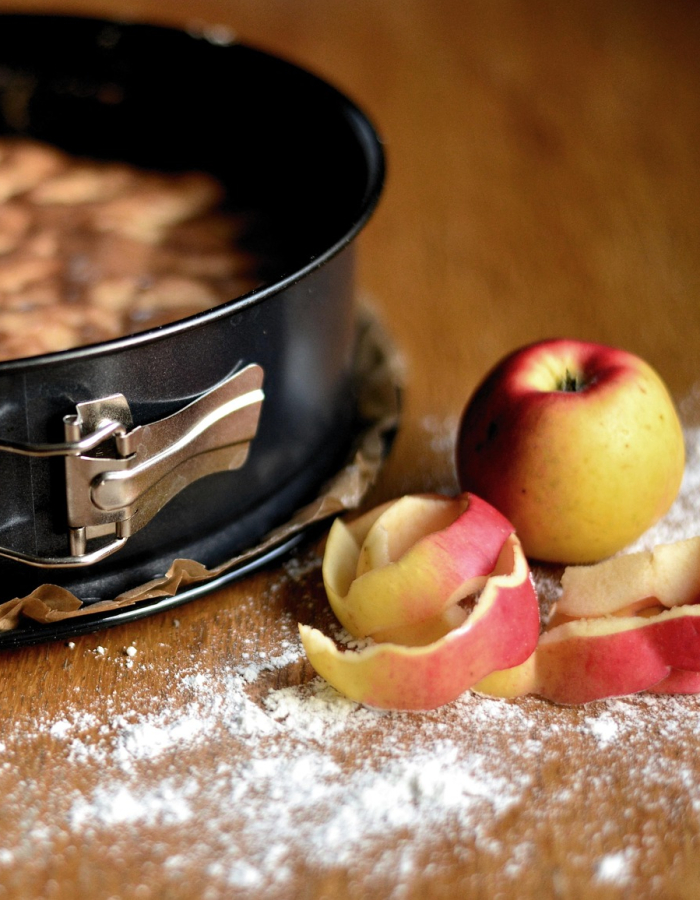 A peeled apple beside an apple cake in a springform pan