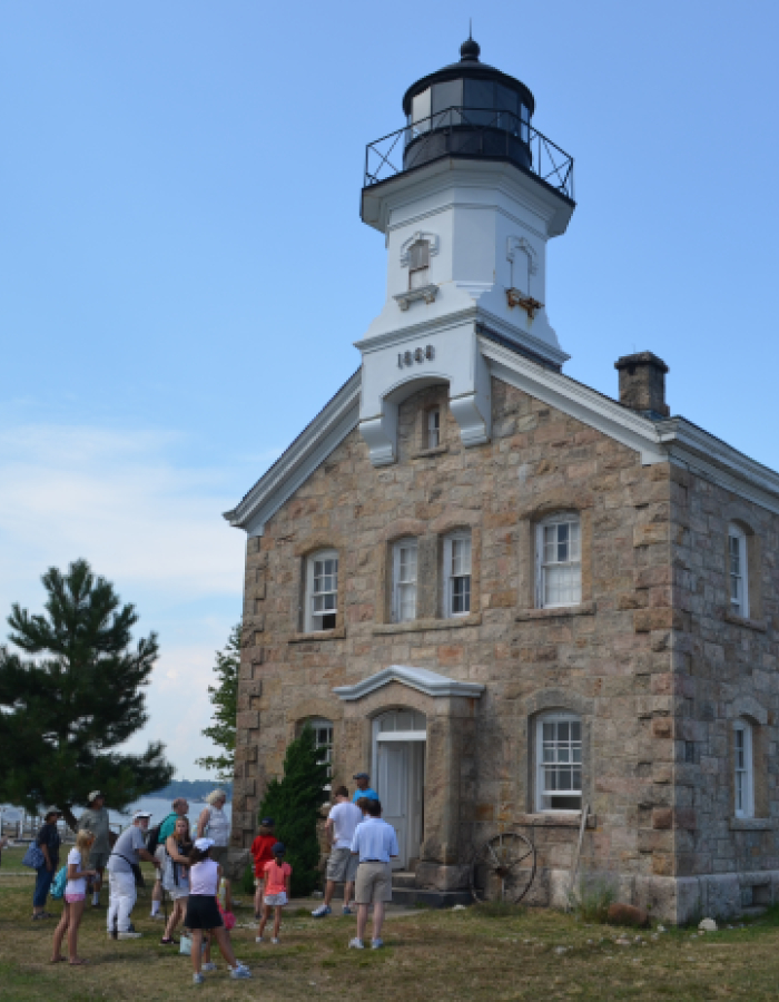 Stone lighthouse with people gathered outside near waterfront