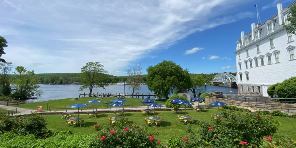 Outdoor seating with umbrellas on grassy lawn by river and white building
