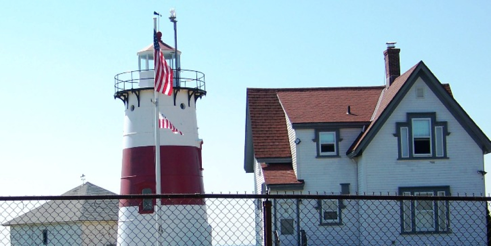 Red and white lighthouse with adjacent white house and American flag