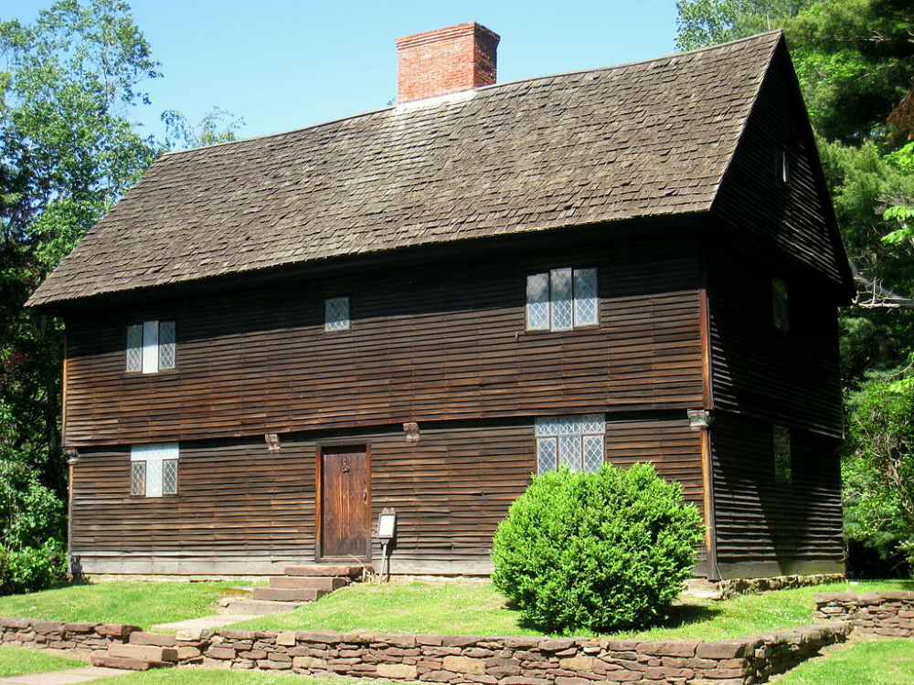 Historic two-story wooden house with diamond-paned windows and stone wall