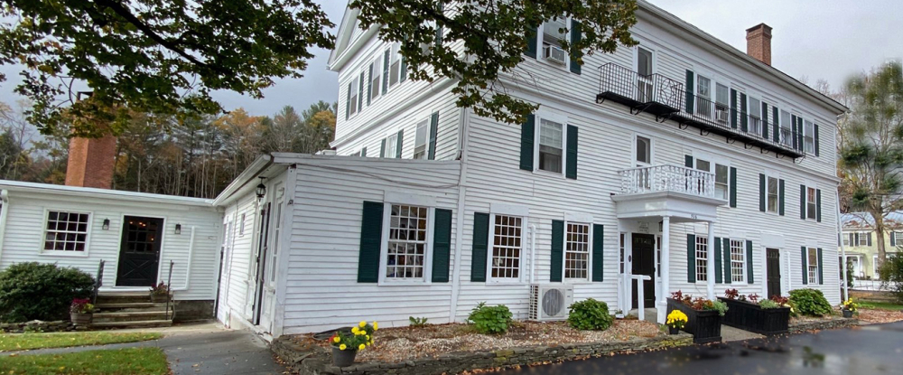 Large white colonial building with green shutters and small garden