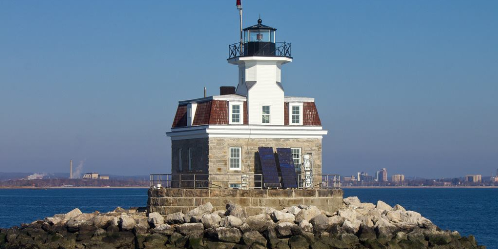 Lighthouse on rocky breakwater with city skyline in background