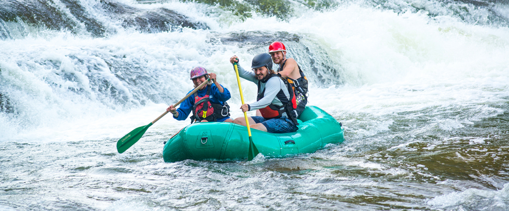 Three people rafting on whitewater river rapids wearing helmets and life jackets