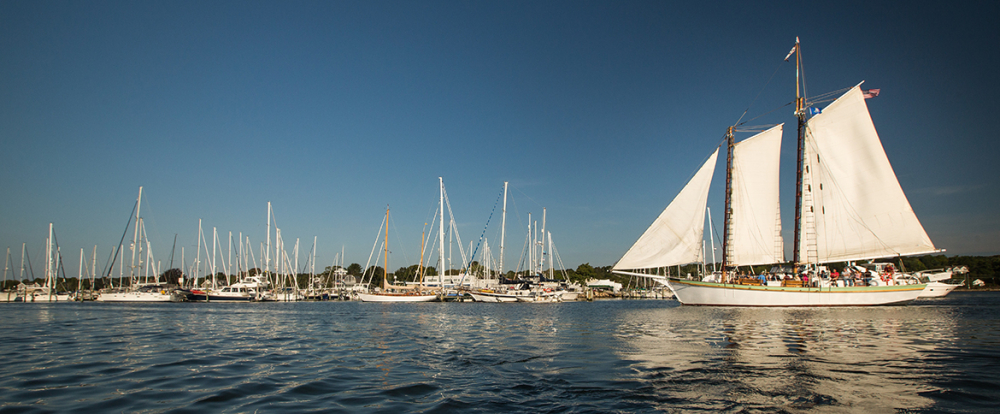 White sailing ship Argia with people on board near marina under blue sky