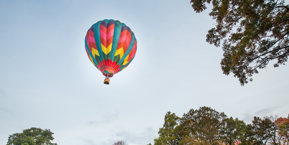 Colorful hot air balloon flying over autumn forest and green field