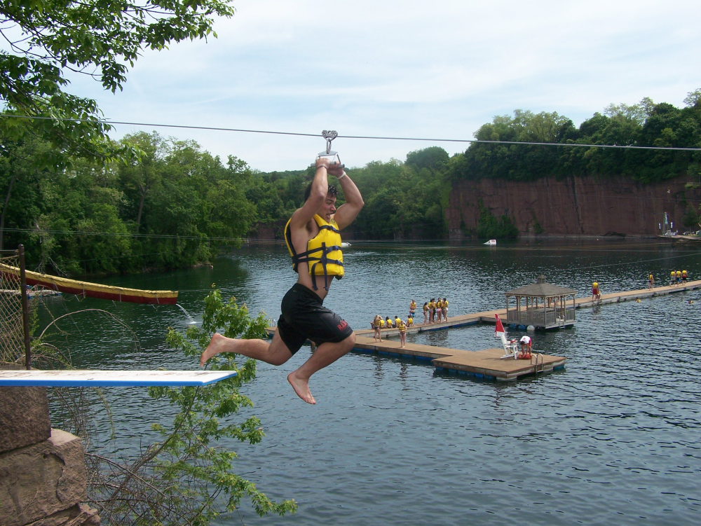 Boy jumping from zip line into lake wearing yellow life vest
