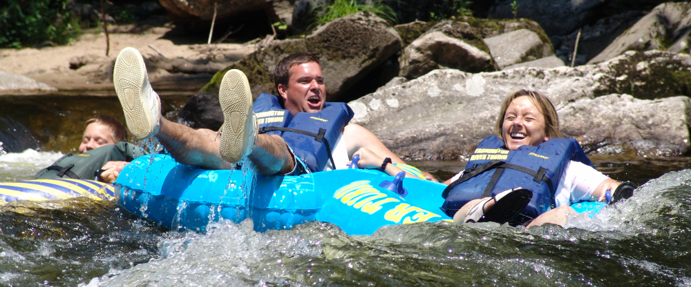 Three people laughing while tubing down a rocky river