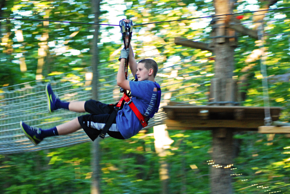 Boy wearing harness and helmet ziplining through forest adventure park