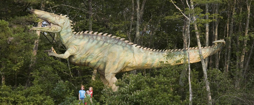 Large dinosaur sculpture with children in wooded Dinosaur Place park