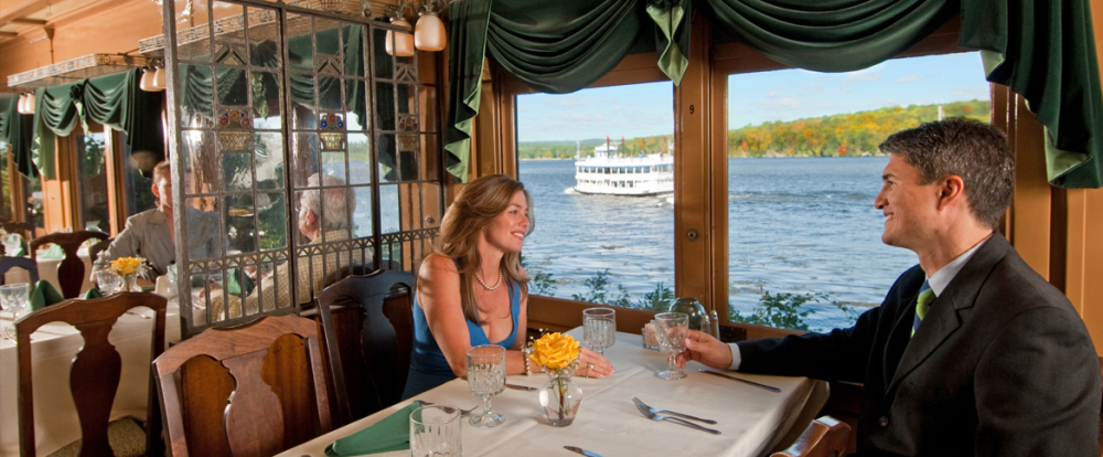 Couple dining inside train with large window showing riverboat outside