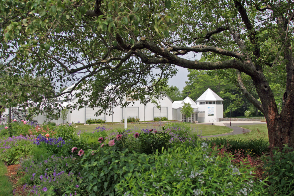 White museum building with pointed roofs behind a garden and trees
