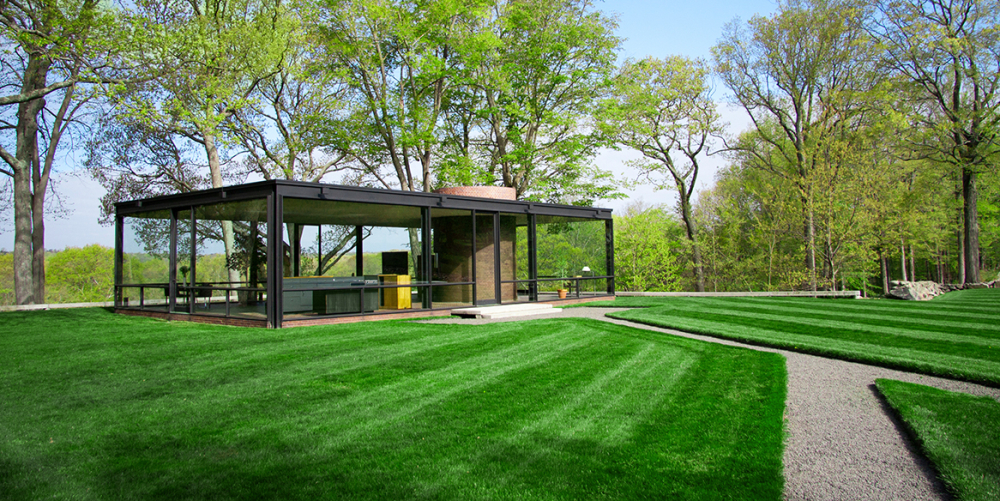 Modern glass house in green lawn surrounded by tall trees