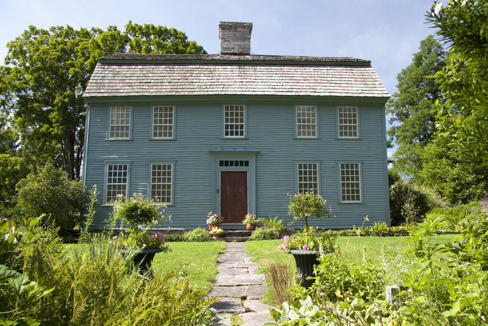Historic blue wooden house with red door surrounded by garden and trees