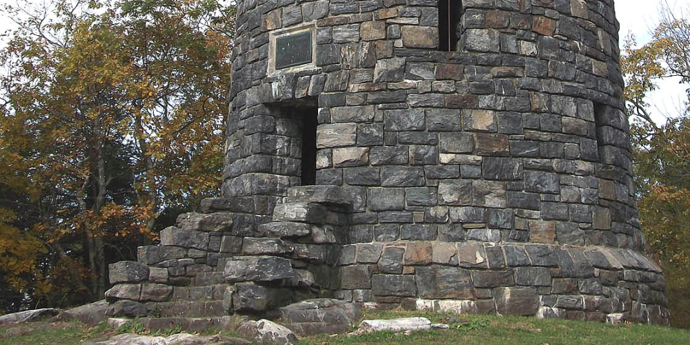 Round stone watchtower with stairs and small windows on grassy hill