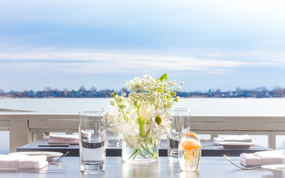 Table setting with white flowers, glasses, and ocean view background