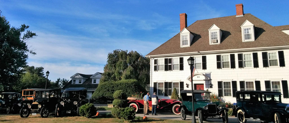 Vintage cars parked by large white colonial inn on sunny day