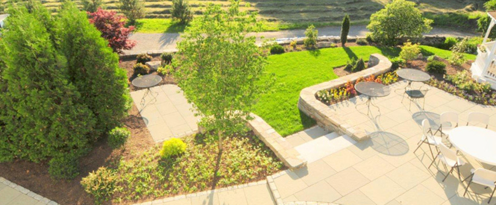 Sunlit garden patio with tables, chairs, and green landscaping