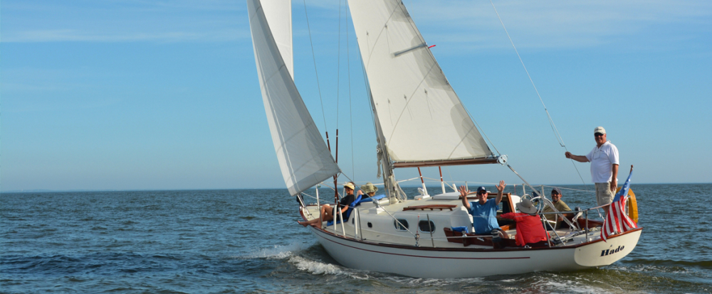Sailboat with six smiling people sailing on calm water under clear sky