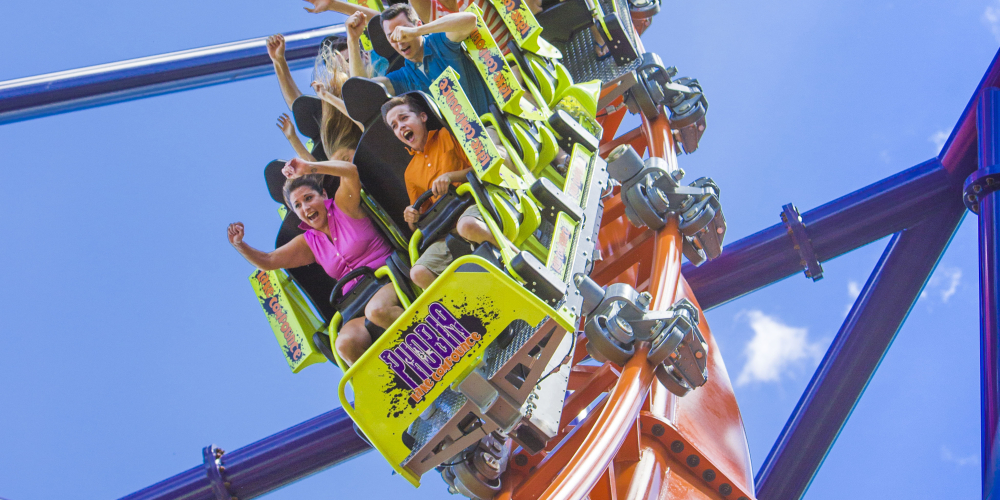 People screaming and raising hands on steep roller coaster drop